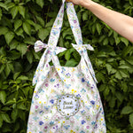 Floral-patterned tote bag held by a hand against a green leafy background
