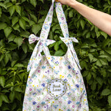 Floral-patterned tote bag held by a hand against a green leafy background