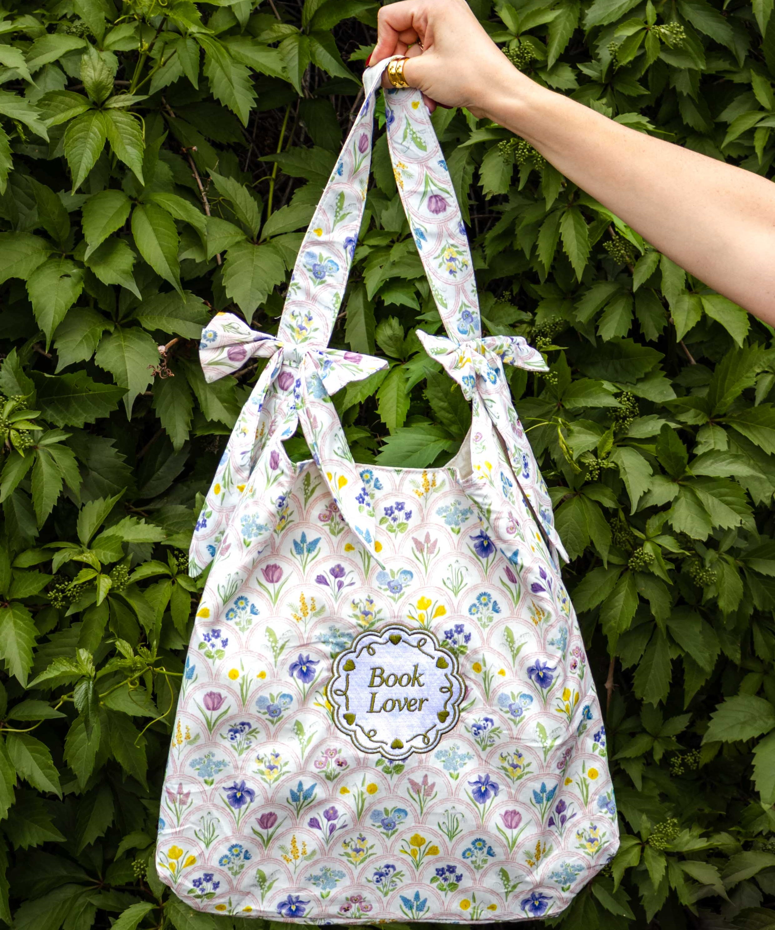Floral-patterned tote bag held by a hand against a green leafy background