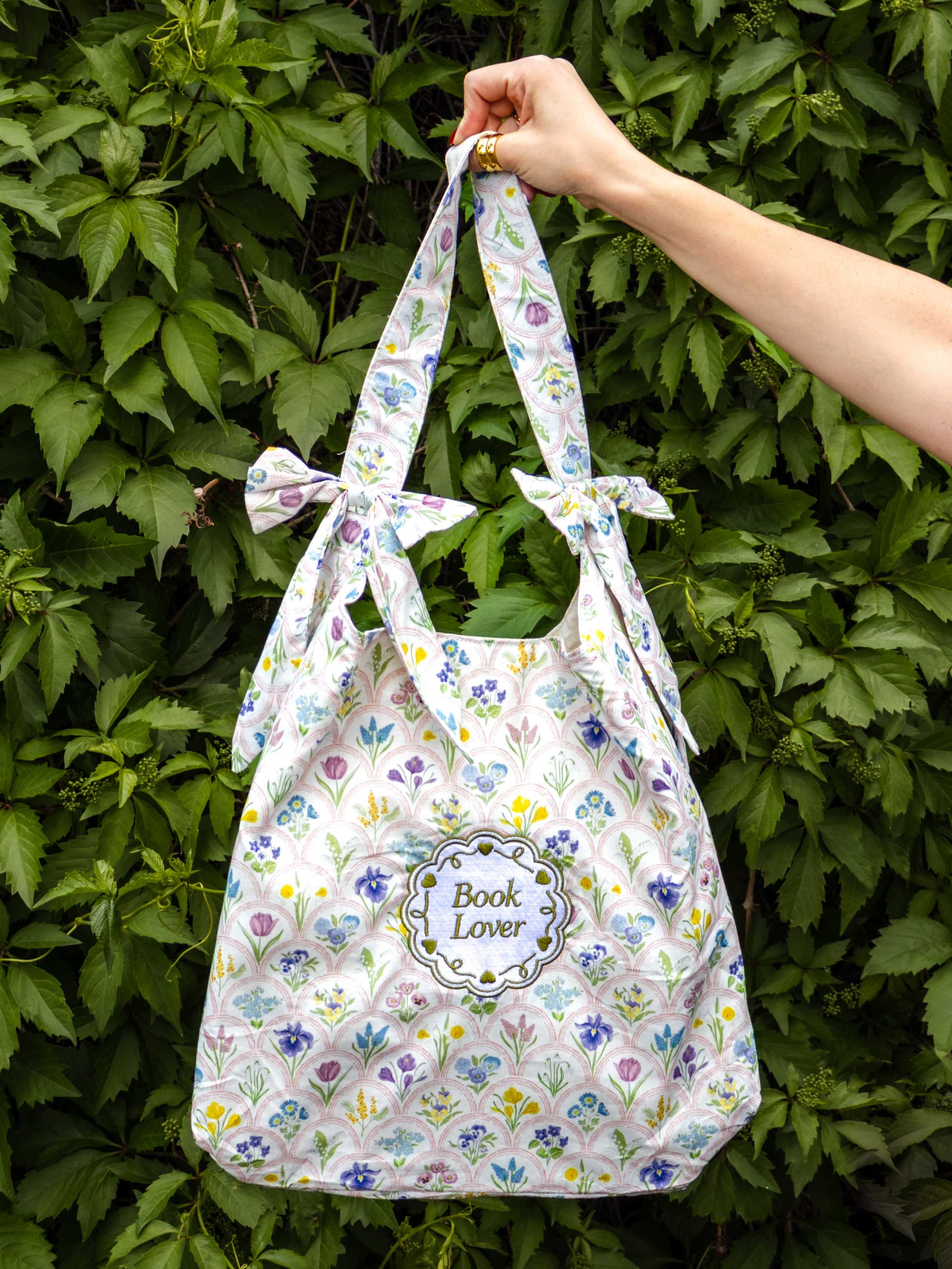 Floral-patterned tote bag held by a hand against a green leafy background