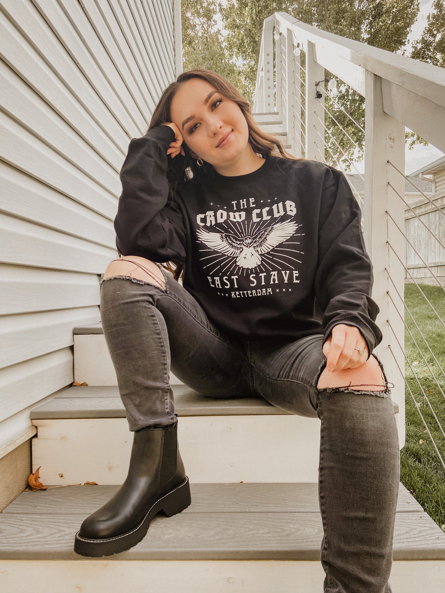 model woman sitting on stairs with crow club sweatshirt on