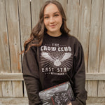 Model woman standing wearing crow club sweatshirt and holding a book