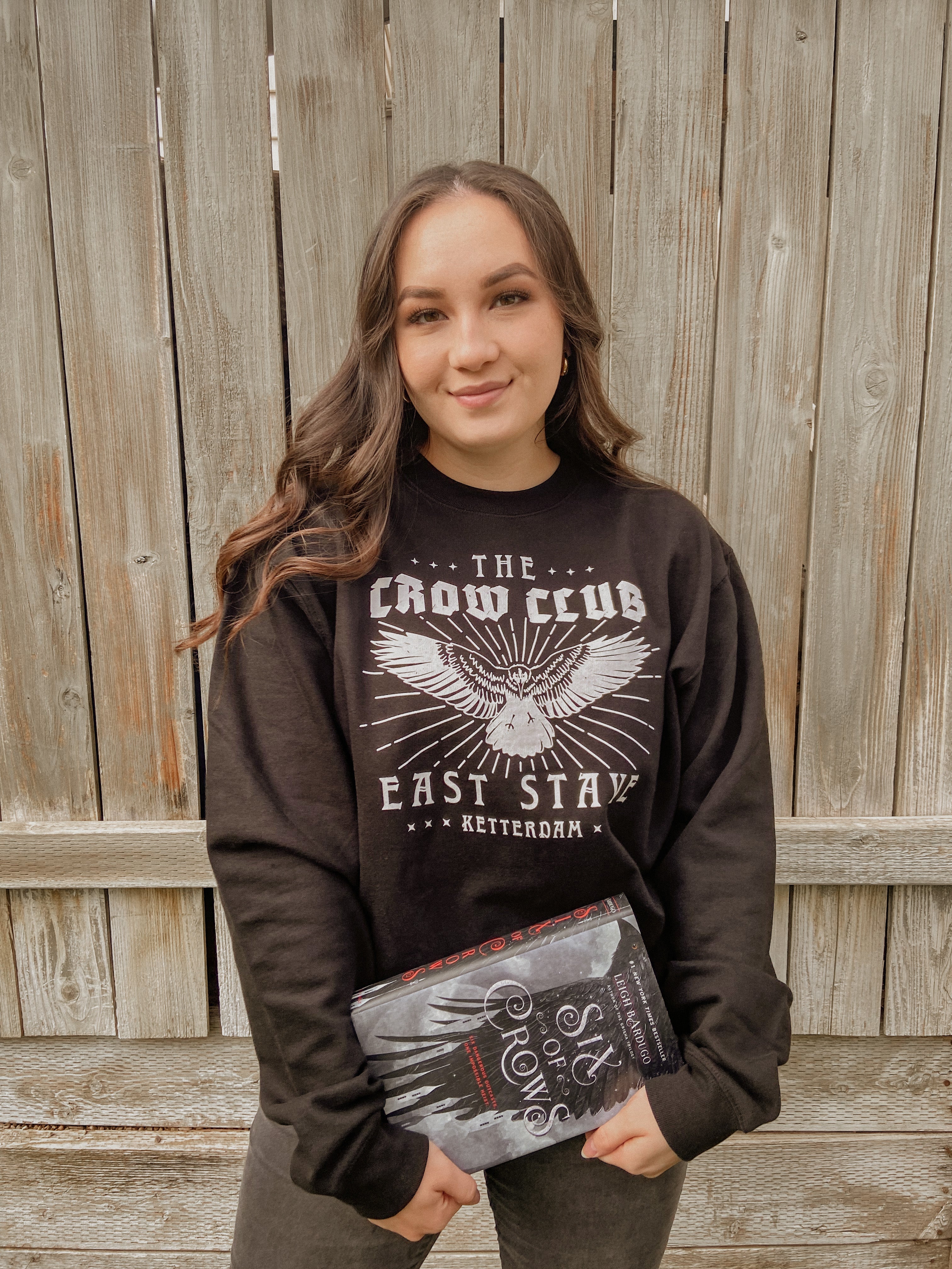 Model woman standing wearing crow club sweatshirt and holding a book